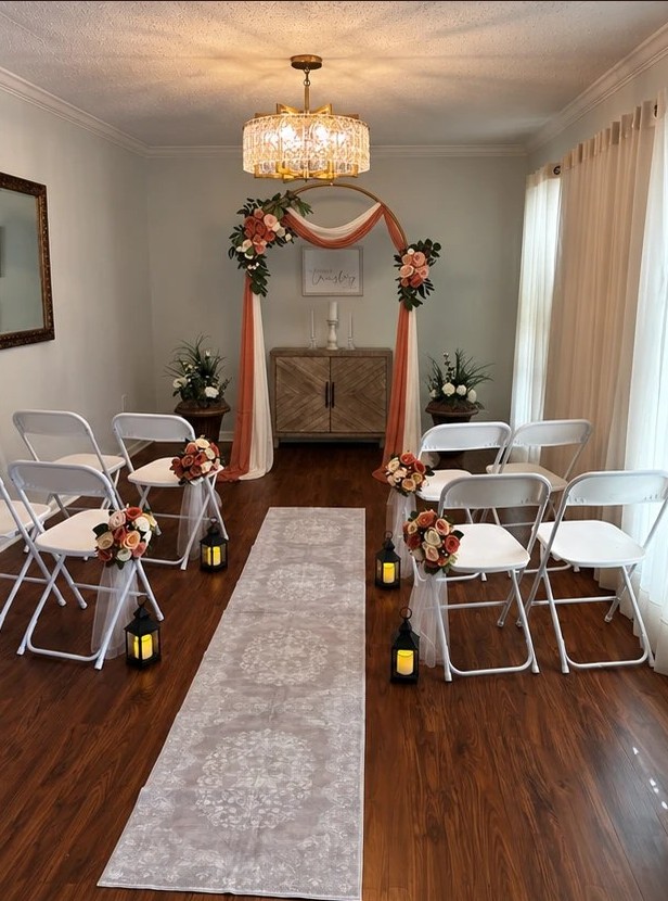 The ceremony room styled for autumn, with a terracotta draped arch, coral and peach flowers, and lanterns along the aisle